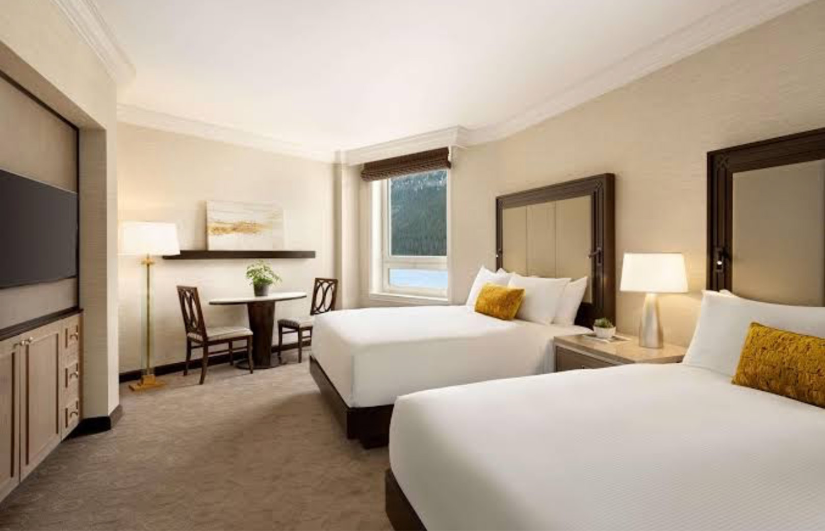 Hotel room with two queen beds, matching headboards, nightstands, lamps, and a window overlooking trees/landscape