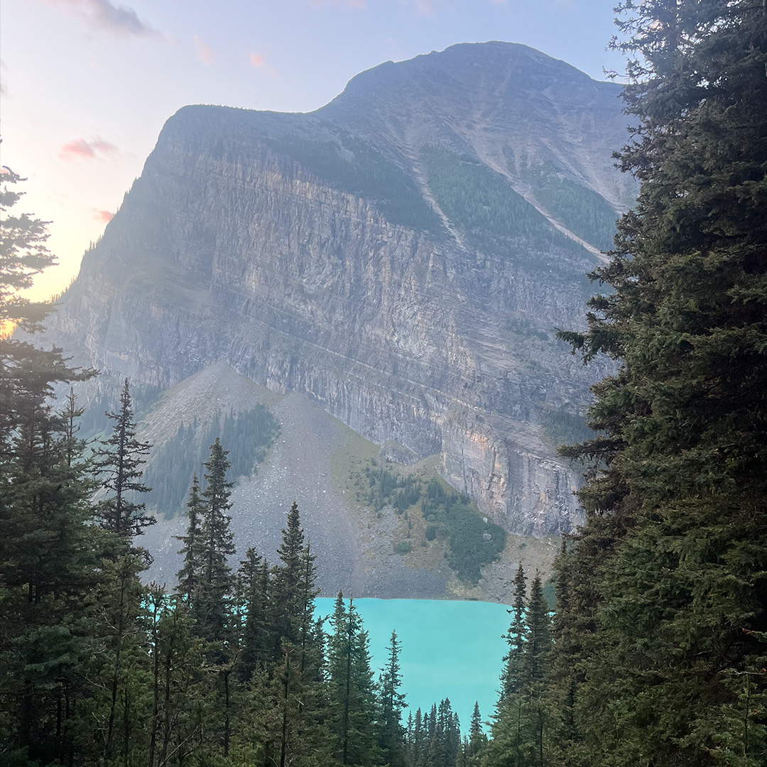 Turquoise alpine lake framed by pine trees with a rocky mountain backdrop at dusk.