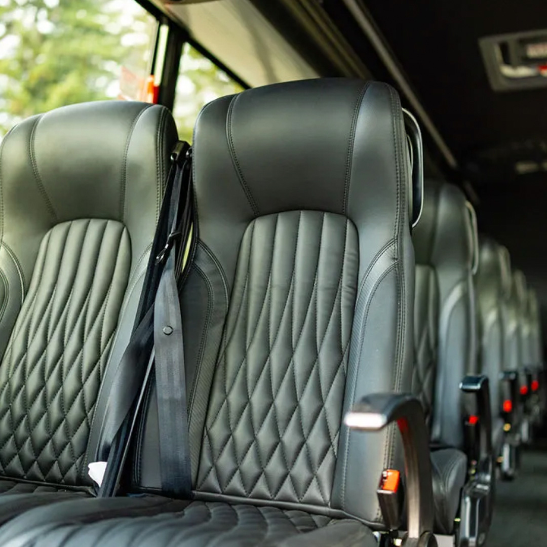 Interior of a bus with black diamond-stitched leather seats and seat belts along a row of seats
