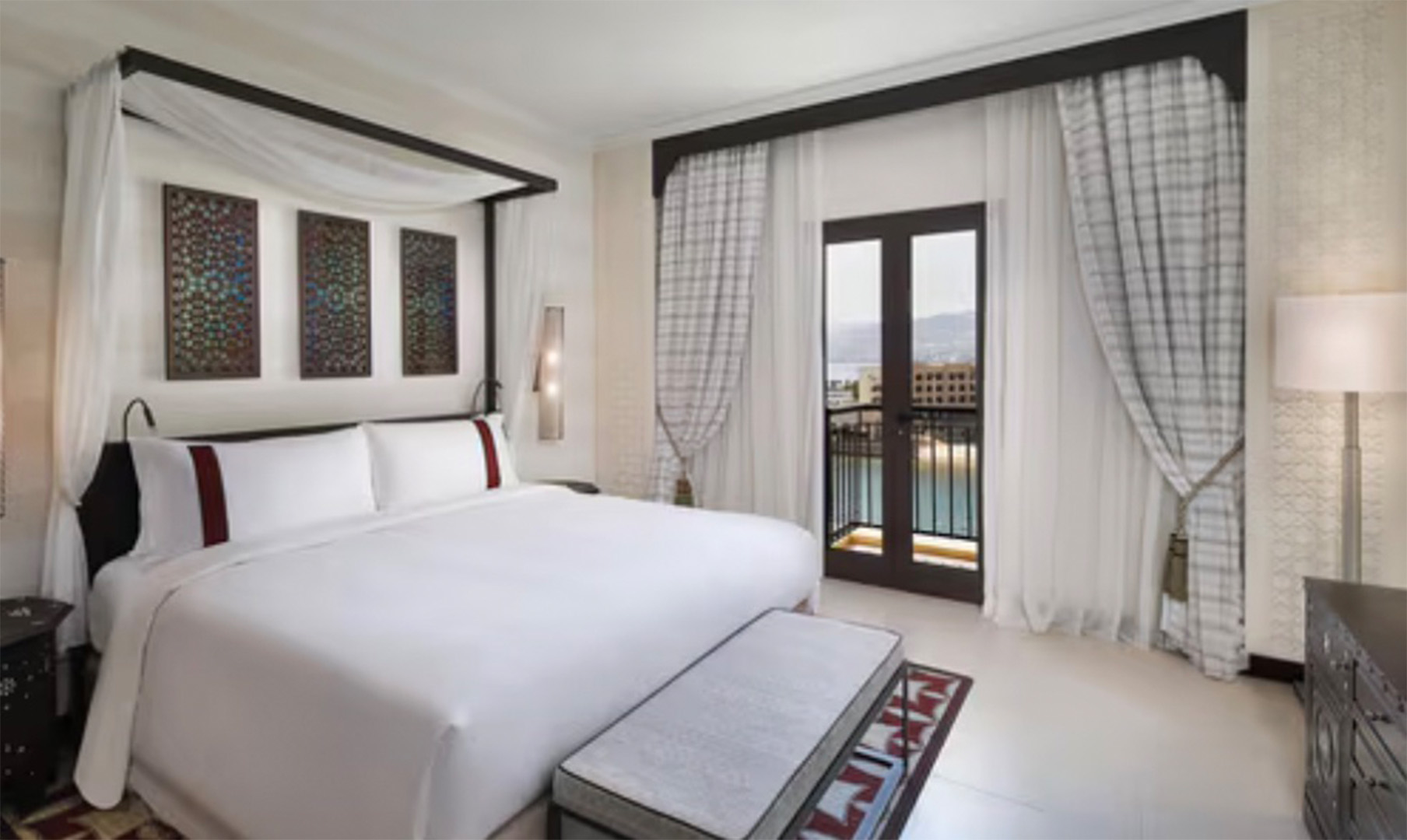 Luxurious hotel bedroom with a white canopy bed, three colorful panels above, and balcony doors with sheer curtains.