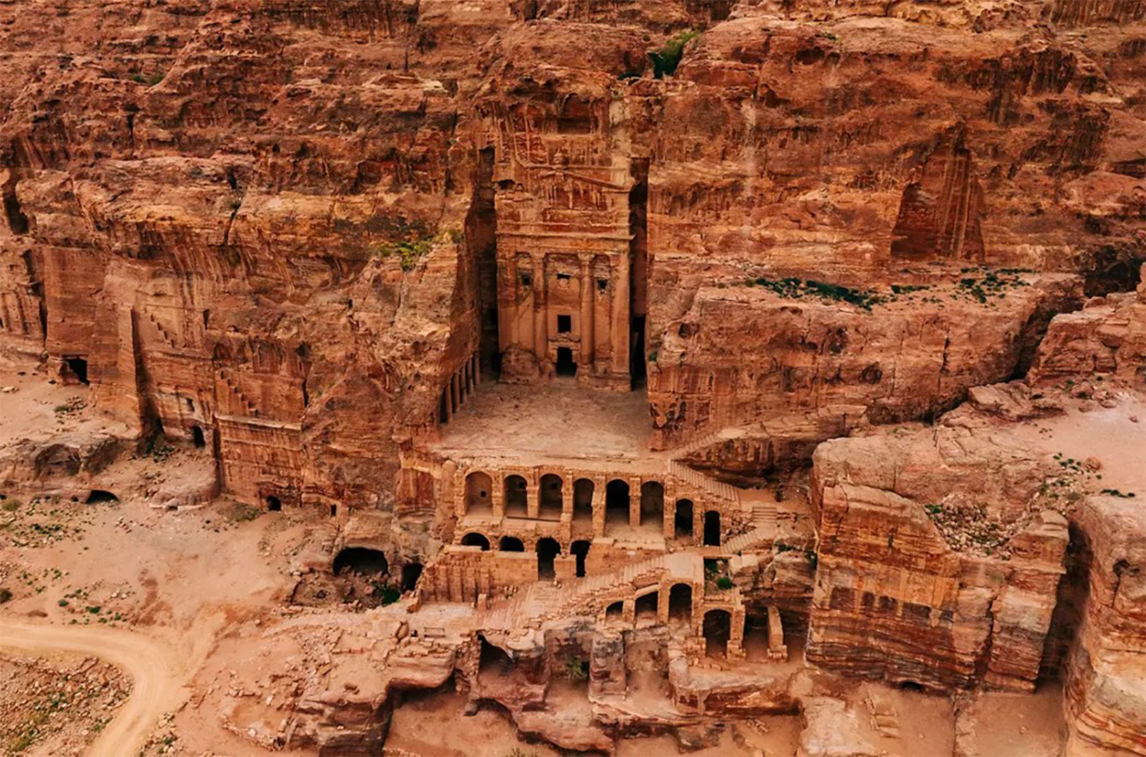 Ancient sandstone cliff facade with a central temple and arched colonnade carved into rock surface on a canyon wall?”